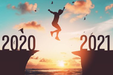 2020 'den 2021' e tropikal günbatımı plajında uçurumun arasında siluet adam zıplıyor. Özgürlük mücadelesi ve seyahat macera tatili konsepti. Klasik ton filtre efekti renk biçimi.