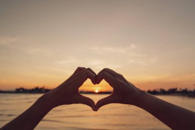 Kadın elleri doğada kalp şeklinde bokeh güneş ışığı dalgası ve tropik tropik günbatımı plaj soyut arka planı. Mutlu aşk yolculuğunun ve doğa konseptindeki özgürlüğün kopyası. Klasik ton rengi.