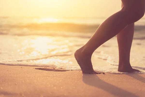 Close up woman legs walking on tropical sunset beach with smooth wave and bokeh sun light wave abstract background. Travel vacation and freedom feel good concept. Vintage tone filter color style.