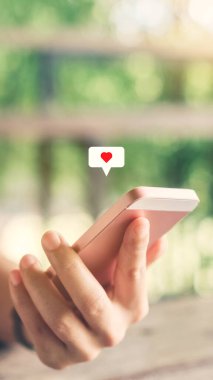 Kafenin arka planında kalp ikonu olan akıllı telefon kullanan bir kadın. Teknoloji işi ve sosyal yaşam tarzı konsepti. Klasik ton filtre efekti renk biçimi.