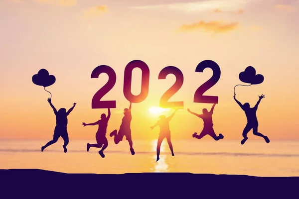 Siluet arkadaşları 2022 'de tropikal plajda soyut gökyüzü arka planında atlayıp tutuyorlar. Mutlu yıllar ve bayram kutlamaları. Klasik ton rengi.