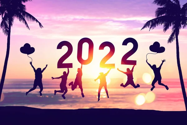 Silhouette friends jumping and holding number 2022 on sunset sky with palm tree abstract background at tropical beach. Happy new year and holiday celebration concept. Vintage tone color style.
