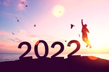 Siluetçi adam atlıyor ve kuşların sayısı 2022 gibi soyut gökyüzünde tropik bir plajda uçuyor. Mutlu yıllar ve bayram kutlamaları. Klasik ton filtresi renk biçimi.