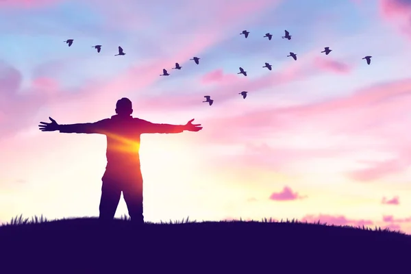 Man rising hands and birds flying on sunset sky at nature field abstract background. Freedom feel good and travel adventure concept. Vintage tone filter effect color style.