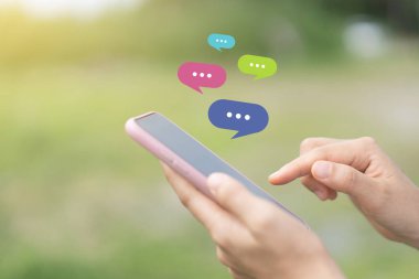 Açık doğa parkı arka planında sohbet ikonu olan akıllı bir telefon kullanarak kadın el ele tutuşunu kapat. Teknoloji ve seyahat tatil konseptinin kopyalama alanı. Klasik ton filtre efekti rengi.