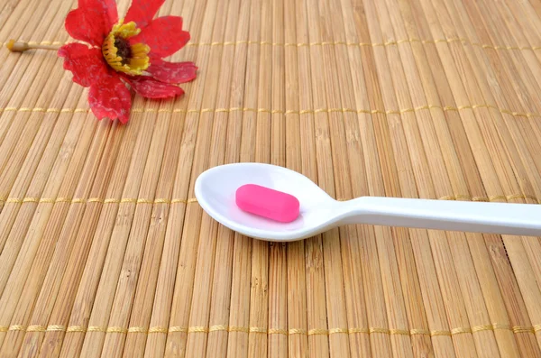 Comprimido de medicamento rosa na colher e flor vermelha — Fotografia de Stock