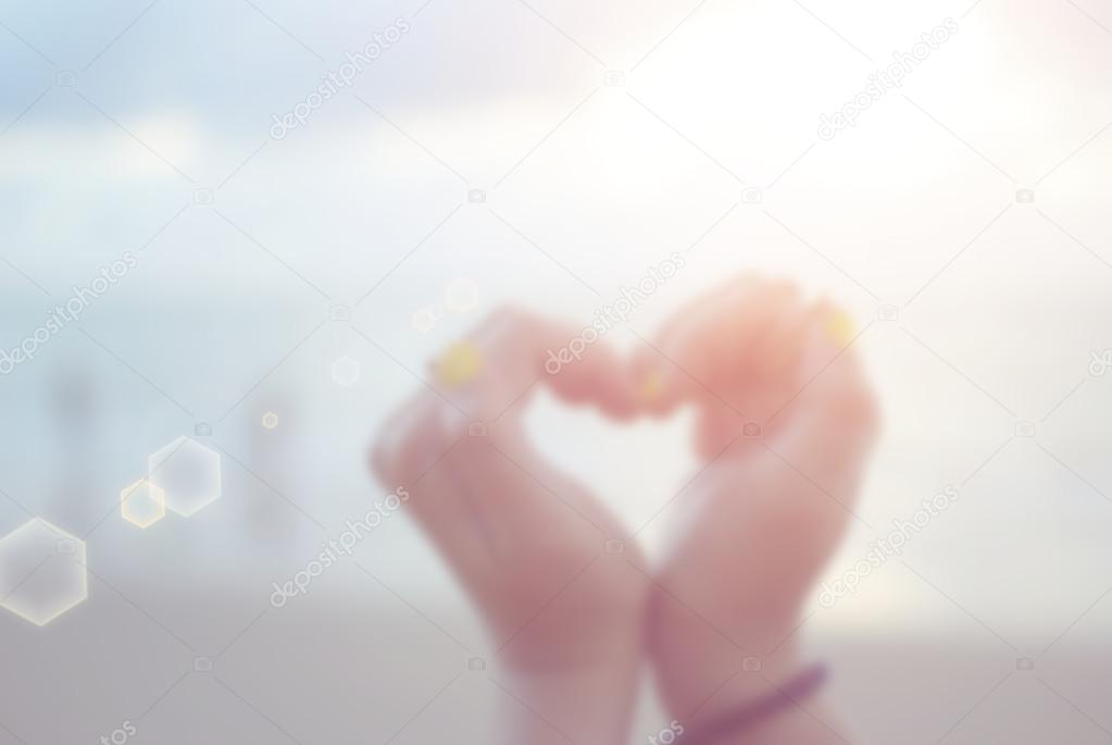 Blur woman hand in shape of heart on sunset beach abstract background.