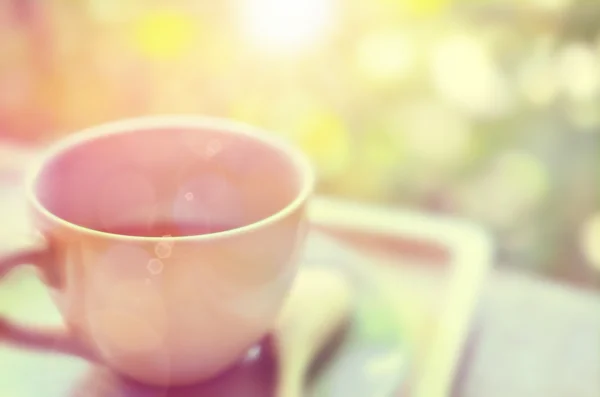 Desenfoque una taza de café en la mesa de madera con bokeh naturaleza verde y luz del sol de la mañana fondo abstracto . — Foto de Stock
