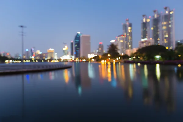 Twilight blur bokeh lights city office building and water reflection — Stock Photo, Image