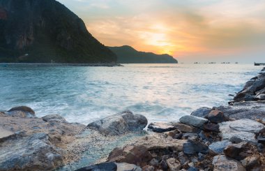 Kayalık plaj ve dağ arka plan üzerinde gündoğumu