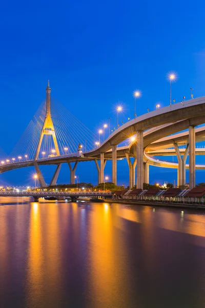 Crepúsculo sobre puente colgante conectar a la carretera frente al río — Foto de Stock