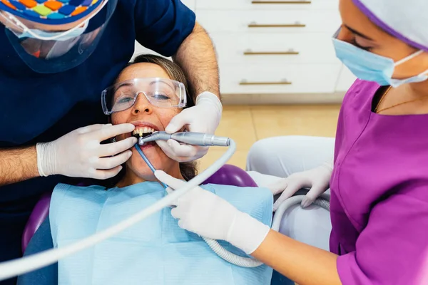 Dentist working in the mouth of a sick patient with tooth pain. The doctor is assisted by his assistant, the young nurse. The dentist is equipped with a mask, latex gloves and a cap. Health concept