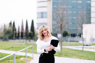 30 yaşında, siyah etek ve beyaz bluz giymiş bir kadının şehir caddesinde dizüstü bilgisayar koluyla yürümesi iş hareketliliği kavramı. yatay fotoğraf kopyalama alanı