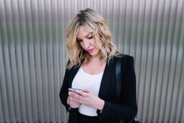 30 yaşında, sarı saçlı, cep telefonuna mesaj yazan bir kadının portresi. Şehrin sokaklarındaki akıllı telefonuyla internete bağlı internet iletişimi. Teknoloji kavramı.