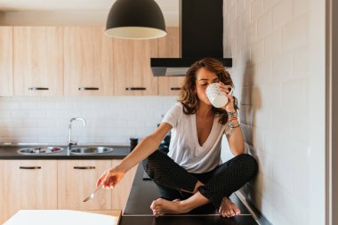 Mutfak tezgahında kahve içen güzel bir kadın. Rahatlamış kız evinde bir fincan çay molası veriyor. Yatay fotoğrafta kopyalama alanı.