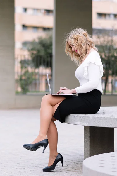 Elegant businesswoman works remotely with laptop on the street. I work on the street connected to the internet. Freelance work concept.