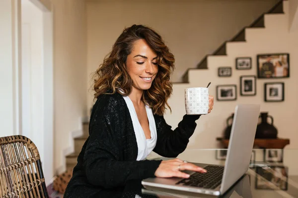 Portrait of a cheerful woman at home with a laptop and a cup of coffee on the table. 30 year old girl connected online to a meeting with friends and family. Telework concept