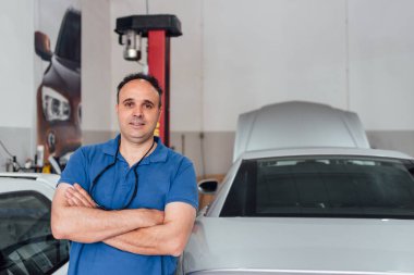 Atölyesindeki mutlu araba tamircisi zarif üniformasıyla poz veriyor..