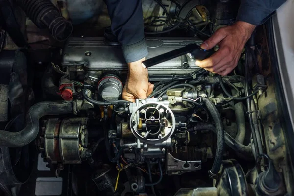 Tamircinin elleri araba motorunu tamir eder. Onarılırken karbüratör açıldı. Servis bakımı.