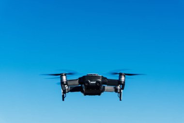 Mavi gökyüzünde uçan beyaz bir dronun genel görüntüsü. Hava gözetimi için uzaktan kumanda ekipmanı.