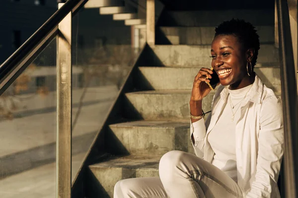 Retrato de uma menina africana de pele preta sentada nas escadas e falando em seu telefone celular — Fotografia de Stock