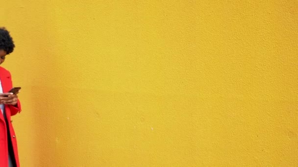 Όμορφη νεαρή μαύρη-skin Afro-American κορίτσι στέκεται με κινητό τηλέφωνο με τα πόδια κάτω από το δρόμο σε κίτρινο φόντο. — Αρχείο Βίντεο