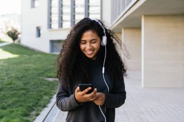 Afro kız cep telefonu ve kulaklığıyla müzik dinliyor.