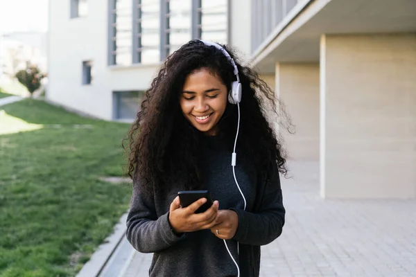 Afro girl ฟังเพลงด้วยโทรศัพท์มือถือและหูฟังของเธอ — ภาพถ่ายสต็อก