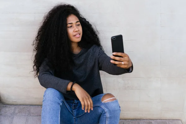 Mladá afro dívka pomocí svého chytrého telefonu sedí venku. — Stock fotografie