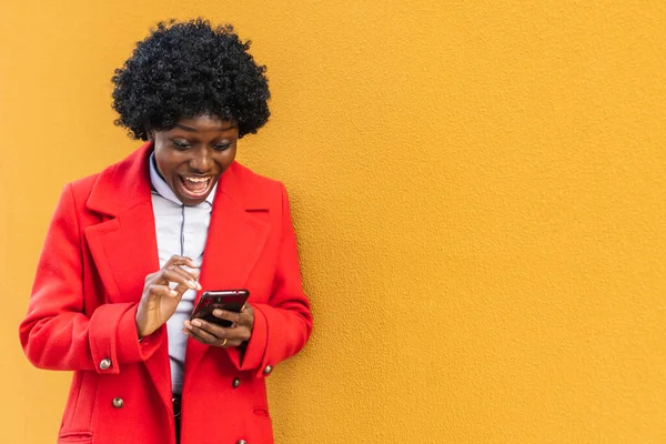 Açık havada, güzel bir gülümsemesi olan, sarı arka planda cep telefonu kullanan, internette cep telefonuyla gezen arkadaşlarına internetten mesaj atan esmer tenli bir kızın fotoğrafı. Boşluğu kopyala
