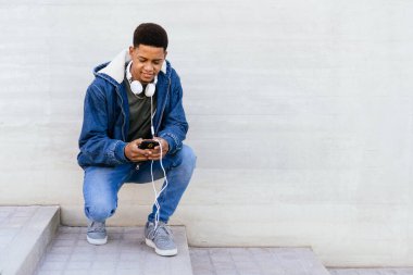 Sokaktaki afro çocuk kulaklıklı cep telefonunu kullanıyor.. 