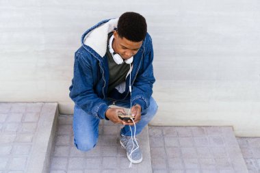 Sokaktaki afro çocuk kulaklıklı cep telefonunu kullanıyor.. 