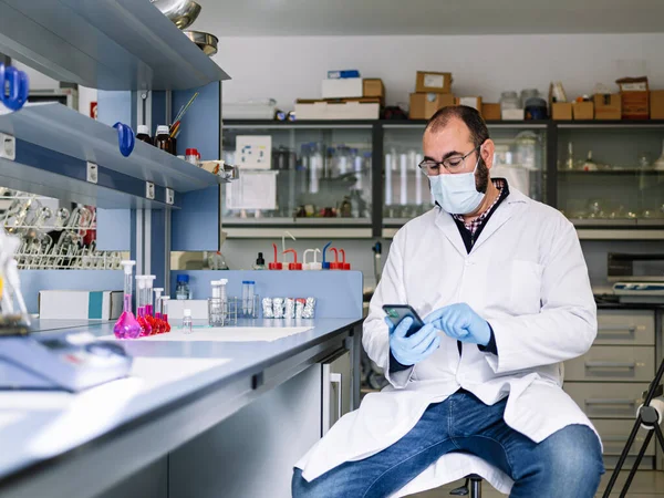 Mężczyzna naukowiec w okulary za pomocą smartfona w laboratorium chemii. — Zdjęcie stockowe