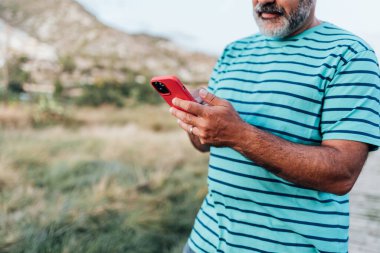 Yetişkin bir adam dışarıda dikilirken akıllı telefonunu kontrol ediyor..