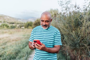 Orta yaşlı bir adam açık havada eğlenirken cep telefonuyla mesajlaşıyor..