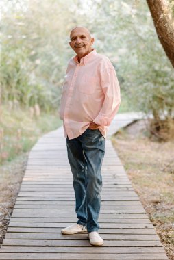 Orta yaşlı bir adam dışarıda tahta bir yolda poz verirken gülümsüyor..