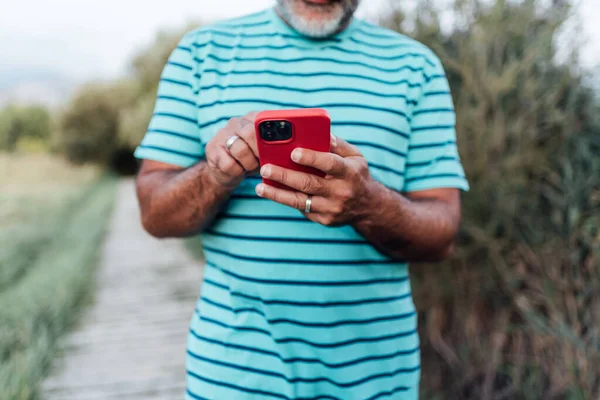 Doğada dikilirken, yetişkin bir adamın cep telefonu kullanışına yakından bakın..