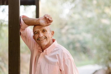 Yetişkin bir adamın kameraya baktığı ve dışarıda bir sütuna yaslanırken gülümsediği görüntüyü kapat..