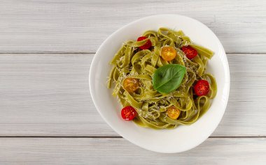 Ispanaklı, kiraz domatesli ve peynirli yeşil makarna, beyaz bir masada, yatay, insan yok.,