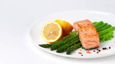 Kızarmış somon balığı, kuşkonmaz ve limon, beyaz bir tabakta, yatay olarak.,