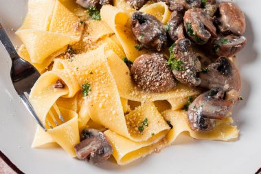 Beyaz bir tabakta servis edilen mantarlı ve kremalı lezzetli pappardelle makarna.