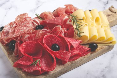 Çeşit çeşit et, aperatif, prosciutto, salam ve jambon, maasdam peyniri ve zeytinlerle ahşap bir tahtada, kahvaltı, üst manzara, yakın çekim, insan yok.