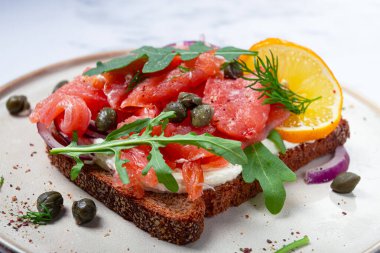 Taze füme somonlu sandviç, siyah ekmek, süzme peynir, otlar ve kırmızı soğanlar, kapariler ve turunçgiller, mermer tezgahta, kahvaltı, insan yok.,