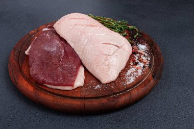 Taze çiğ ördek göğsü, ahşap kesim tahtasının üzerinde, bitkiler ve baharatlarla, insan yok.
