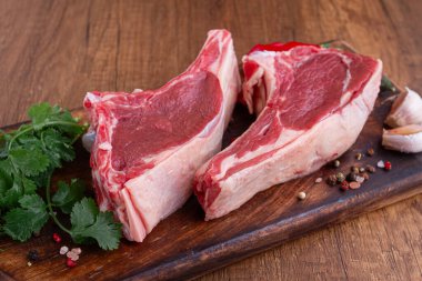 Taze kesilmiş kuzu pirzolası, otlar ve sebzelerle ahşap bir tahtanın üzerinde, pişirmeye hazır, ahşap bir masada.,