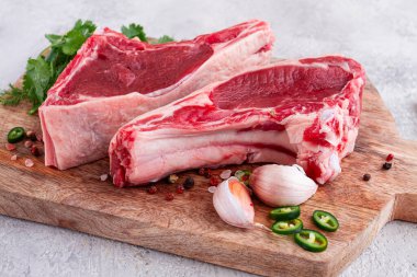 Kemiğin üzerinde taze et parçaları, ahşap bir kesim tahtasının üzerinde, bitkiler ve baharatlarla, mutfakta pişirmeye hazır.