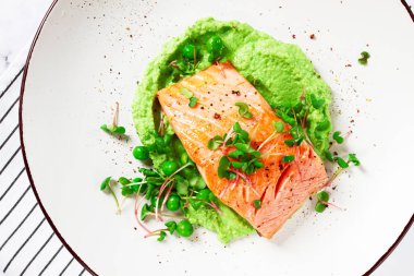 Lezzetli ızgara somon, kremalı yeşil bezelye püresinin üzerine güzelce yerleştirilir. Taze mikroçerezler ve bezelyeler her yemek için mükemmel bir iştah açıcı yemek oluşturan parlak bir dokunuş ekler..