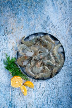 Taze çiğ karides, limon ve mermer bir yüzeyde kişniş dilimleri ile buza yayılmış, pişirmeye hazır, insan yok.