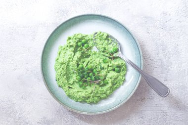 Canlı yeşil bezelye püresi taze bezelye ve mikroyeşilliklerle kaplı sığ bir kaseyi doldurur. Yemek taze ve davetkar görünüyor. Hafif ve besleyici bir yemek için her zaman ideal..