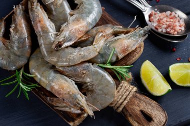 Taze çiğ, beyaz ayaklı karides, kaplan karidesleri vannamei, tahta kesme tahtasında, limon dilimleri ve baharatlarla,